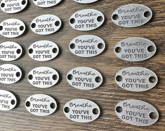 May include: A collection of 16 silver oval-shaped metal tags with the text "Breathe You've Got This" engraved on each tag.
