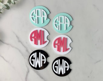 May include: Six round coasters with different monogram initials. The coasters are in three colors: white, black, and light blue. The monograms are in pink, white, and black.