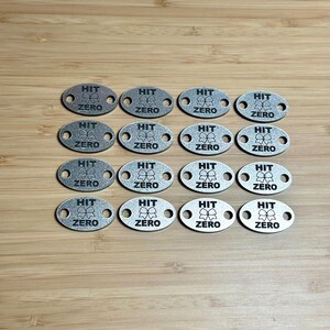 Könnte beinhalten: Eine Sammlung von 16 silberfarbenen Metall-Etiketten mit dem Text "HIT ZERO" und einer kleinen Schleifengrafik.