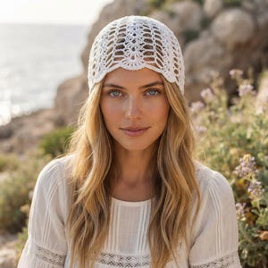 May include: A white crochet beanie featuring an intricate, openwork lace pattern with a scalloped edge. The headwear is crafted from fine white yarn, showcasing a detailed, repeating geometric design that covers the crown and sides of the head.