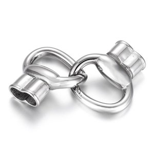 May include: Silver-toned metal clasp with a heart-shaped design. The clasp is made of two interlocking loops.