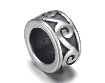 May include: A silver bead with a decorative, swirling pattern. The bead is cylindrical with a large central hole and a polished finish. The design features interconnected, curved lines and spirals. The bead is suitable for jewellery making.