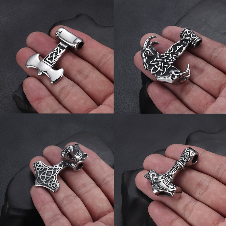 May include: Four silver pendants with intricate designs. The pendants feature a hammer, a wolf head, a goat head, and a knot. The pendants are all made of metal and have a shiny finish.