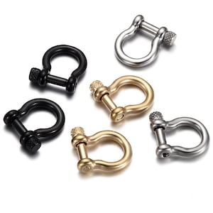 Puede incluir: Cinco anillos en D de metal de diferentes colores con un cierre de tornillo texturizado. Los anillos en D son negros, plateados, dorados y dos tonos de plata.