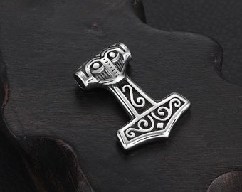Może przedstawiać: Srebrny wisiorek Mjolnir z misternymi, wirującymi wzorami. Wisiorek ma szczegółową główkę młota z wypukłym wzorem i pętlą na górze do przymocowania do łańcuszka.