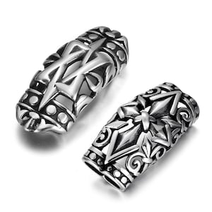 May include: Two silver metal hair tie charms with intricate designs. One charm features a stylised cross with a crown at the top. The other charm features a stylised arrow with a floral design.
