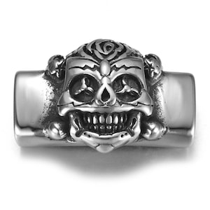 Könnte beinhalten: Silberfarbener Metall-Schädel-Anhänger mit detailliertem Design, inklusive einer Rose und gekreuzten Knochen. Der Schädel hat ein zahniges Grinsen und komplizierte Augendetails.