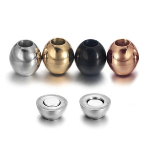 May include: Four spherical beads in silver, gold, black, and copper colors are displayed. Two additional silver-colored magnetic clasps are also shown. These beads are likely components for jewelry making or craft projects.