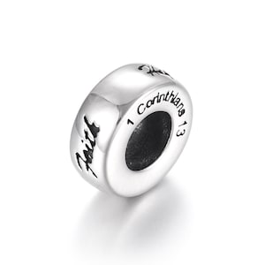 Może przedstawiać: Srebrna koralikowa zawieszka z wygrawerowanym słowem "Wiara" i tekstem "1 Koryntian 13".