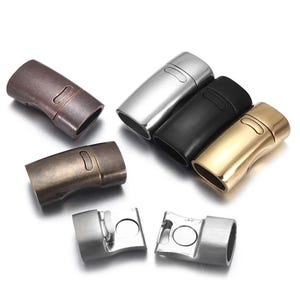Pode incluir: Uma variedade de fechos magnéticos em vários acabamentos metálicos, incluindo bronze, prata, preto e dourado. Os fechos são cilíndricos com um design curvo e uma ranhura para fixação. Dois fechos são mostrados abertos, revelando os componentes magnéticos.