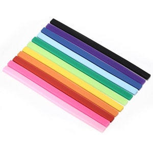 Puede incluir: Un conjunto de diez reglas de plástico de colores, dispuestas en forma de arcoíris, con la regla negra en la parte superior y la regla rosa en la parte inferior.