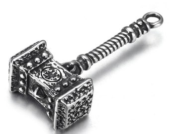 May include: A silver-toned metal pendant in the shape of a hammer with a twisted handle. The hammer head has a detailed design with a circular pattern in the centre.