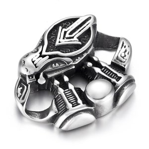 May include: Silver-toned pendant featuring an intricate design of a building with a downward-pointing arrow. The pendant has a smooth, round surface on the underside.