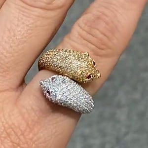 以下が含まれることがあります： 2つのリング。1つは金色のリング、もう1つは銀色のリングで、それぞれ小さな動物の形をしており、表面はテクスチャ加工されています。 金色のリングには、目の赤いアクセントがあります。 リングは指にあります。