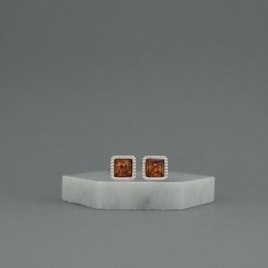 May include: A pair of silver earrings with square amber stones set in a beaded border.