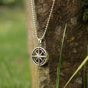 Op de afbeelding: Een zilveren ketting met een ronde kompas hanger. Het kompas heeft een zilveren frame en een bruin centrum met een zilveren ster.