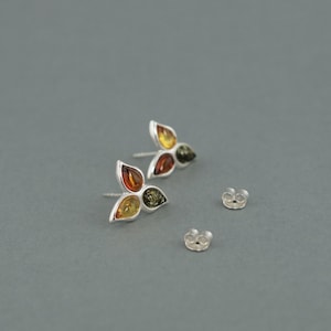 May include: A pair of silver earrings with three amber stones in each earring. The stones are a mix of yellow, orange, and green.