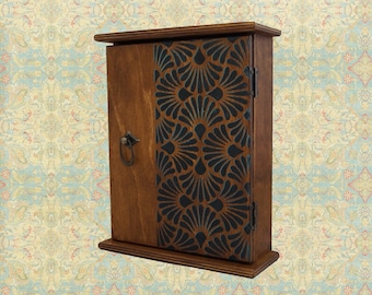 May include: A wooden key holder with a dark brown finish and a black and blue geometric pattern on the front door. The key holder has a metal ring handle and a small shelf at the bottom.