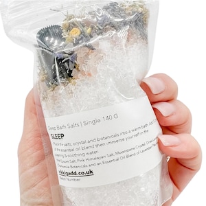 Peut inclure: Un sac en plastique transparent rempli de sels de bain, de plantes et de cristaux. L'étiquette indique "Sleep Bath Salts | Single 140 G". Contient du sel d'Epsom, du sel rose de l'Himalaya et un mélange d'huiles essentielles de lavande.