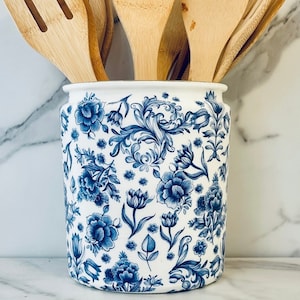 May include: A white ceramic utensil holder with a blue and white floral pattern, filled with wooden spoons and spatulas.