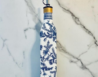May include: A white ceramic oil and vinegar bottle with a blue floral pattern and a gold top. The bottle has a spout for dispensing oil or vinegar.