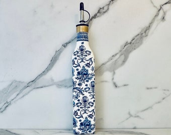 May include: A white ceramic oil bottle with a blue and white floral pattern. The bottle has a silver spout and a gold top.