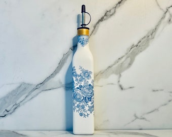 May include: White ceramic bottle with a blue floral design and a gold top. The bottle has a silver pour spout.