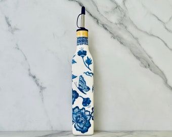 May include: A white ceramic bottle with a blue and white floral design and a butterfly. The bottle has a gold top and a black pour spout.