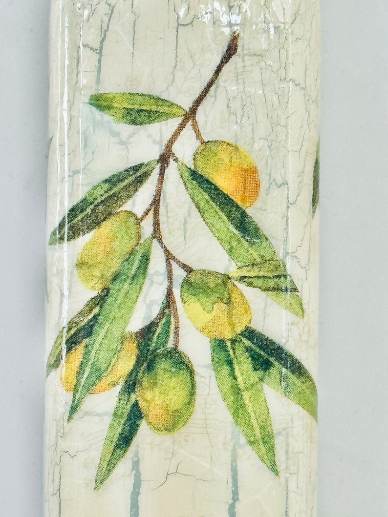 Puede incluir: Una botella de cer&aacute;mica blanca con un acabado desgastado presenta un dise&ntilde;o impreso de ramas de olivo verdes con aceitunas amarillas.