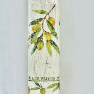 Puede incluir: Una botella blanca con un acabado desgastado presenta un dise&ntilde;o de ramas de olivo con hojas verdes y aceitunas amarillas. La botella tiene el texto "ILES OLIVES NO" y "ILES OLIVES TO" impreso en ella.
