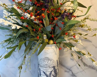 May include: A floral arrangement in a white vase with a lavender design. The bouquet includes white, green, and red berries. The vase has text that reads "Botanists Repository" and "Vol. 1."