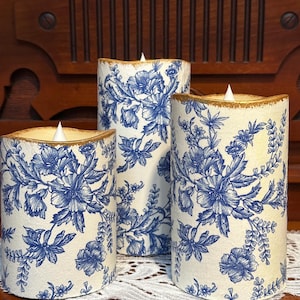 May include: Three white pillar candles with a blue and white floral pattern. The candles have a gold trim around the top and bottom.