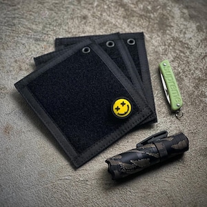 May include: Four black velcro patches with a yellow smiley face patch on the top patch. A green pocket knife and a camouflage flashlight are also in the image.