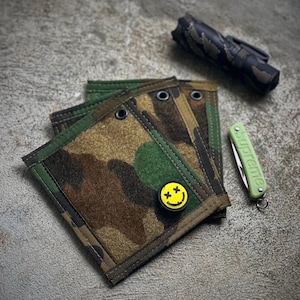 May include: Four camouflage fabric pouches with black stitching and a yellow smiley face pin with black eyes and an 'X' on each eye.