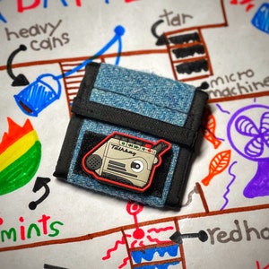 May include: A blue denim wallet with a black trim and a red and black cassette tape patch that says "Talkbay" on it.