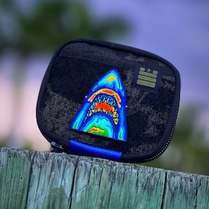May include: A black zippered pouch with a blue and orange shark tooth graphic and a green patch with a star.