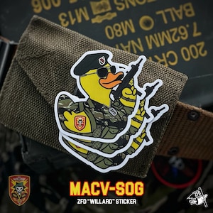 May include: A white sticker with a cartoon duck wearing a camouflage uniform and a black beret. The duck is holding a rifle and has a serious expression on its face. The sticker says "MACV-SOG" and "ZFD "WILLARD" STICKER" in red letters.