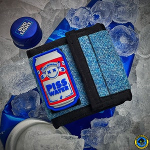 May include: A blue textured fabric wallet featuring a rubber patch of a beer can with the text PISS WATER and a smiley face with X eyes. The wallet is surrounded by ice cubes and a blue Bud Light bottle cap is visible in the upper left corner.