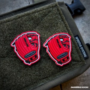 May include: Two red baseball glove patches with black details and white outlines are displayed on a green textured surface. The text "SOOO A400" is visible on each glove. The patches are accessories.