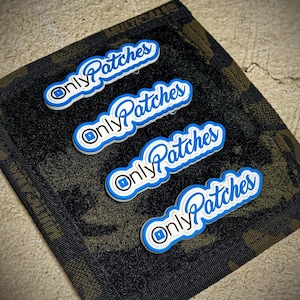 May include: Four white patches with blue lettering that reads "Only Patches" on a dark green fabric background.