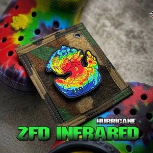 May include: A rubber patch featuring a duck graphic with a rainbow thermal infrared color pattern, positioned on a camouflage fabric square between two tie-dye clogs. The patch includes the text ZFD and the image text reads HURRICANE ZFD INFRARED.