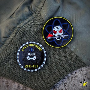 May include: Two black enamel pins with white and yellow accents. One pin features a cartoon duck with a skull and crossbones, the other pin features a cartoon monster with the text "Ugly Duckers ZFD-151".