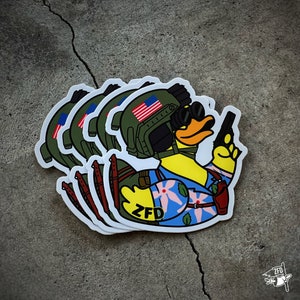 May include: A set of four stickers featuring a cartoon duck wearing a military helmet with an American flag, a floral shirt, and holding a gun. The duck is wearing a backpack and has the letters "ZFD" on its chest.