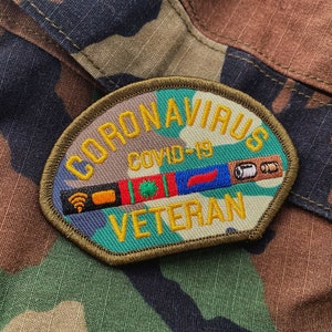 May include: A green, yellow, blue, and red embroidered patch with the text "Coronavirus COVID-19 Veteran" in yellow thread. The patch has a camouflage pattern and features symbols like a wifi signal, a pill, and a red pepper.