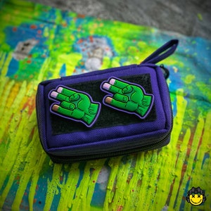 May include: Purple zippered pouch with two green hand patches. The hands are making the 'rock on' gesture with pink fingernails.