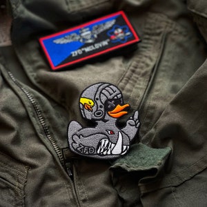 May include: A gray, embroidered patch of a cartoon duck wearing a helmet and sunglasses, with the text "ZFD" on the bottom. The duck is giving the middle finger.
