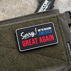 May include: A black patch with white border and the text "Sorry! We're making America Great Again" in red, blue, and white lettering.