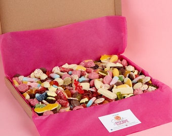 Puede incluir: Una caja de cartón con un forro de papel de seda rosa está llena de una variedad de caramelos coloridos. La caja está abierta y los caramelos son visibles. La caja tiene una pegatina que dice "Sweet Tooth Fairy".
