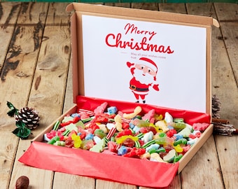 May include: A cardboard box filled with colorful candies and a red-lined interior. A card inside reads "Merry Christmas" with a Santa Claus illustration. The candies are various shapes and colors, including red, green, yellow, and blue.