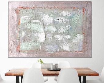 Puede incluir: Pintura abstracta con un aspecto texturizado y en capas. La pintura presenta tonos de gris, blanco y verde, con un sutil borde naranja. La pintura se muestra en una pared sobre una mesa de madera con sillas blancas.